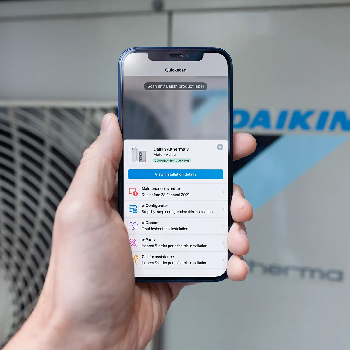 The Daikin application in the hands of an installer showing the actions that can be taken after scanning the QR code of the device. The actions contain maintenance, configuring, troubleshooting, ordering spareparts or calling for assistance.