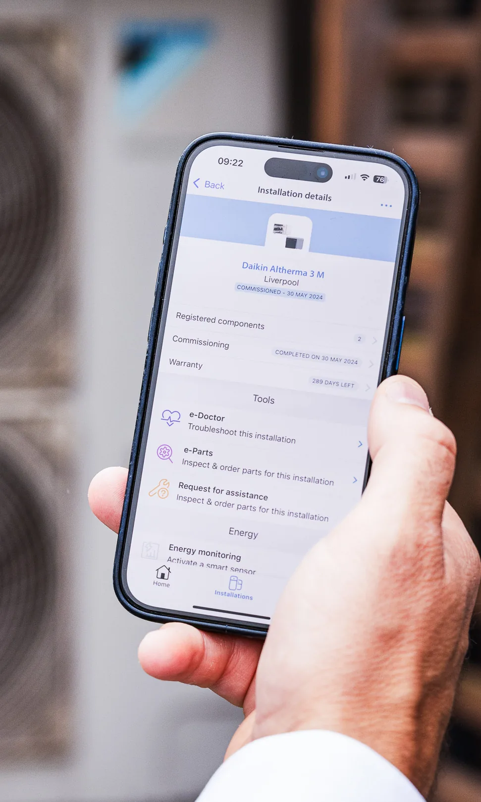 An installer holding a phone showing a heat pump’s installation details, warranty and troubleshooting tools