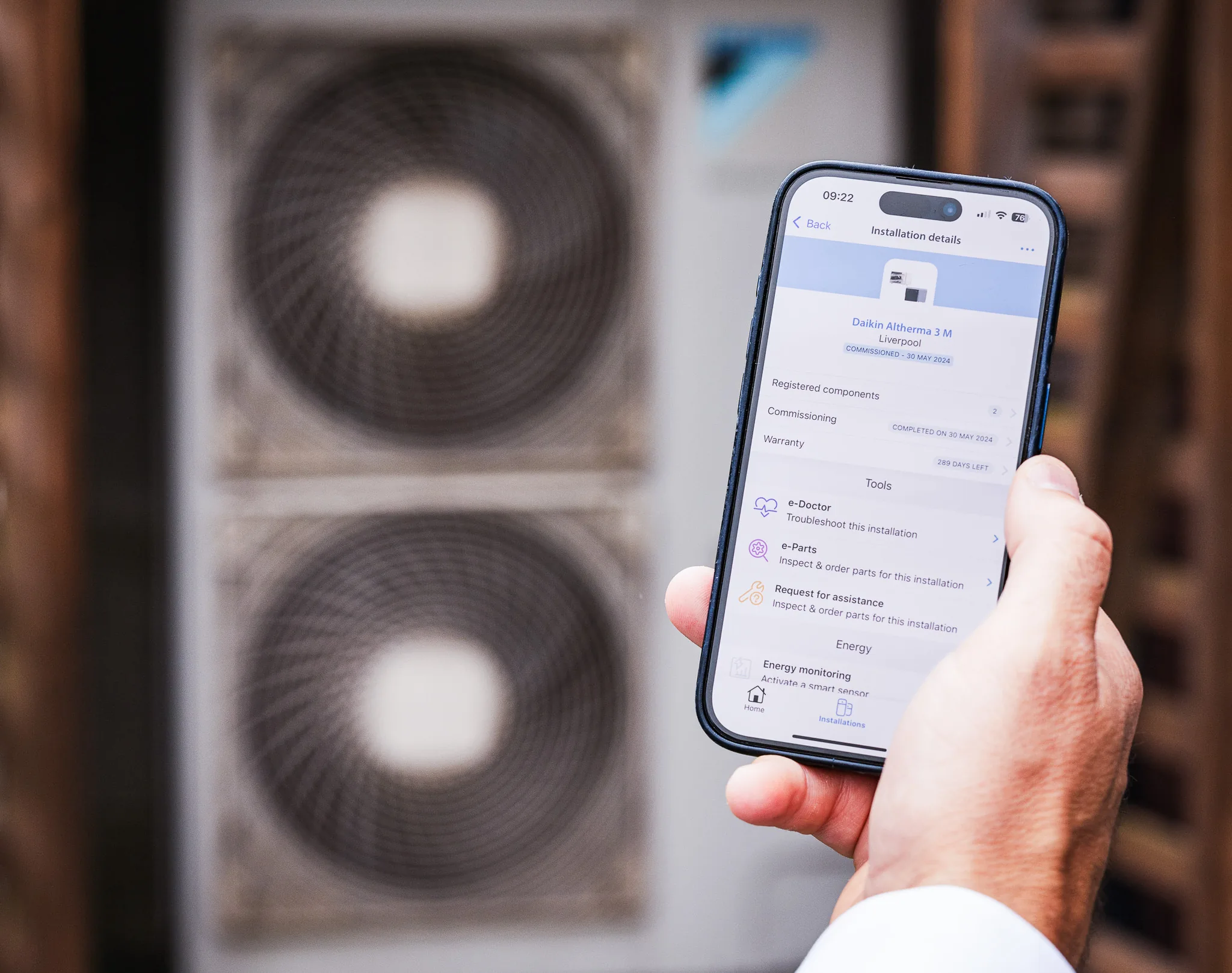 An installer holding a phone showing a heat pump’s installation details, warranty and troubleshooting tools